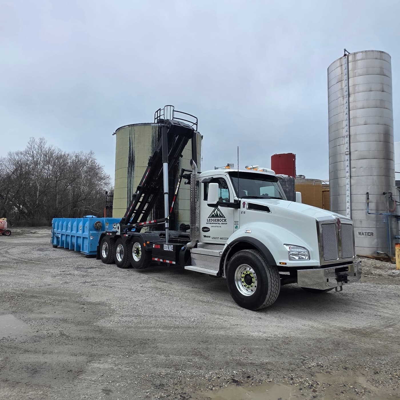 Ledgerock branded truck with blue roll-off containers at industrial site