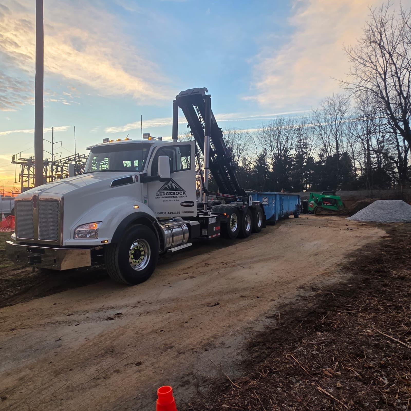 Ledgerock branded truck with roll-off containers at job site, sunset lighting